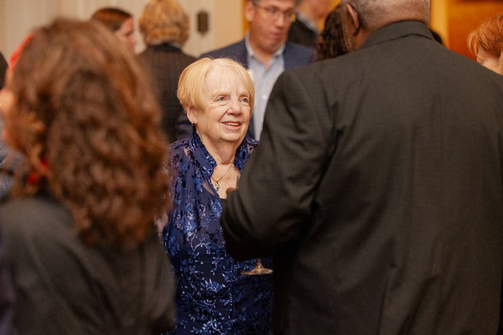 Woman attending reception wearing a sparkly blue shirt, speaking with other guest
